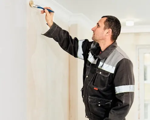 Meseriaș care dă cu grund pe perete înainte de tapetare, într-o cameră luminoasă